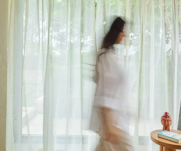 Woman adjusting elegant sheer curtains in a bright room