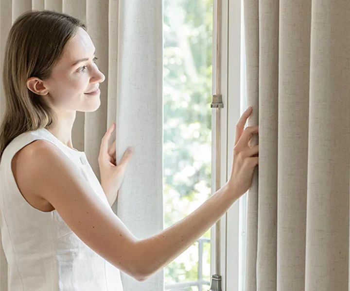 Woman opening luxurious lined curtains by a window
